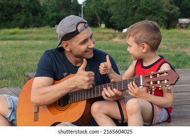 Father Shows His Son How To Play Guitar Outside. They Look At Each Other And Show Thumbs Up. Family Concept