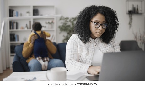 Father sitting with a baby while mother is working on laptop, parental leave - Powered by Shutterstock