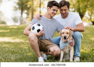father sitting near teenager son with football cuddling golden retriever