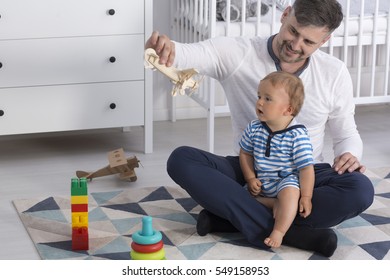 Father sitting on the floor with his child and showing him a wooden plane