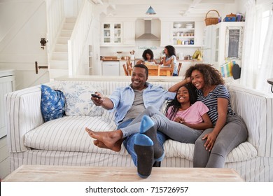Father Sitting On Sofa Watching TV With Teenage Daughters