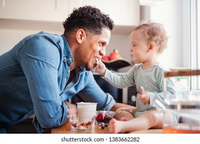 A Father And A Small Toddler Son Eating Fruit And Yoghurt Indoors At Home.