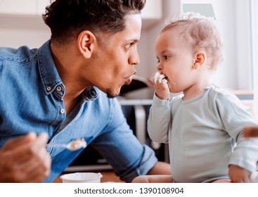 A Father And A Small Toddler Son Eating Fruit And Yoghurt Indoors At Home.