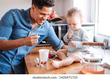 A Father And A Small Toddler Son Eating Fruit And Yoghurt Indoors At Home.