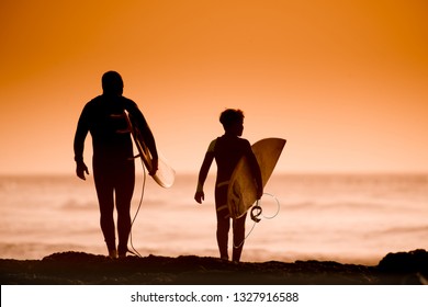 Father and son at the beach with surf. Family scene of a young male with kid enjoying the ocean waves. Silhouette of two man with board standing on the seashore looking the sea. Dad and child together - Powered by Shutterstock