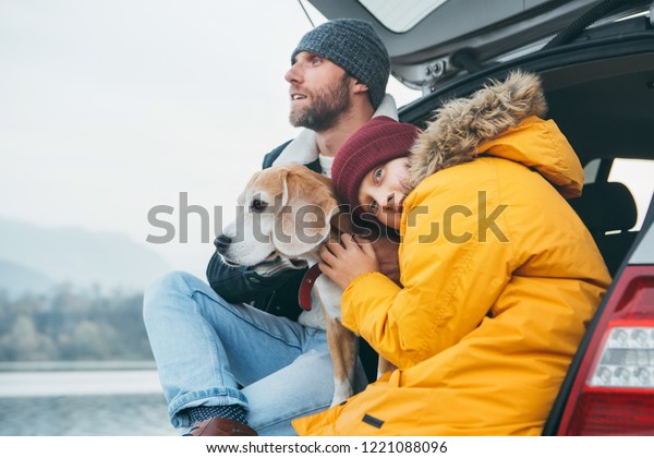 Father and son with beagle dog siting together in\
car trunk. Late autumn\
time