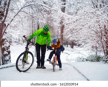 Father And Son With Bicycles In A Winter Park. Father Explains How To Ride A Bike. Weekend In The Winter Park