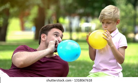 Father and son blowing up balloons, having fun together, carefree recreation