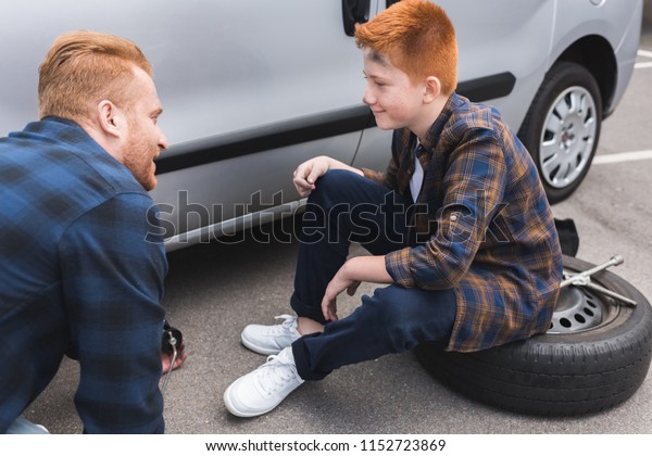 father and son changing tire in car with floor jack\
and looking at each\
other