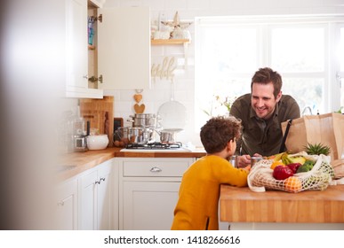 Father And Son Coming Home From Shopping Trip Using Plastic Free Bags Unpacking Groceries In Kitchen