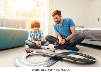 Father and son compete in races with children's cars. They play together on the floor in their house. This is a children's toy. - Powered by Shutterstock