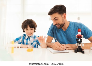 Father and son conduct chemical experiments at home. They use a microscope, flasks, chemical liquids. This is homework to school.