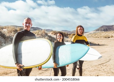 Father, son and daughter getting ready to go surfing in the sea- People wearing wetsuits to go into the water - Three friends walking on the beach - Powered by Shutterstock