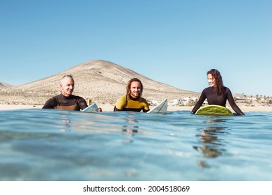 Father, son and daughter sitting on the surfboard in the sea- People wearing wetsuits in the water - Three friends enjoying great time in the water - Powered by Shutterstock