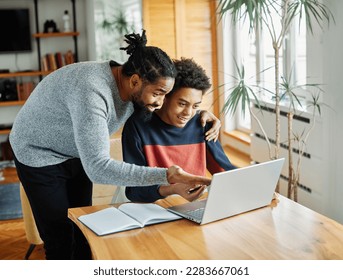 Father and son doing homework with laptop at home. Father and teenage son using laptop. Boy and dad sitting at home working with notebook