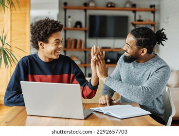 Father and son doing homework with laptop at home. Father and teenage son using laptop. Father and son giving high five hand to each other. Teamwork and cooperation concept - Shutterstock ID 2292657703