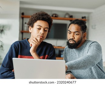 Father and son doing homework with laptop at home. Father and teenage son using laptop. Boy and dad sitting at home working with notebook - Powered by Shutterstock