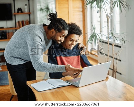 Father and son doing homework with laptop at home. Father and teenage son using laptop. Boy and dad sitting at home working with notebook