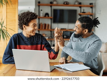 Father and son doing homework with laptop at home. Father and teenage son using laptop. Father and son giving high five hand to each other. Teamwork and cooperation concept