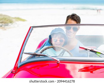 Father And Son Driving Convertible On Beach