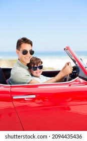 Father And Son Driving Convertible On Beach