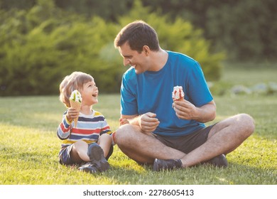 Father and son eating ice cream in waffel cone and fave fun. Laughing family sitting on grass in city park. Happy fathers day. - Powered by Shutterstock