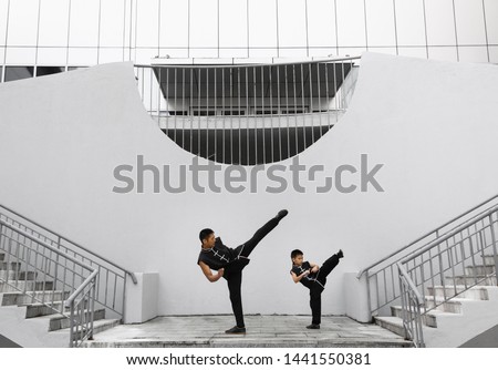 Father and son are engaged in Wushu in the city. The photo illustrates a healthy lifestyle and sport. The father trains the son.