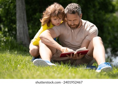 Father and son enjoy spending quality time reading books outdoors. Portrait of father and son relax on green lawn in summer park and read book together. Father and his little son reading book in park. - Powered by Shutterstock