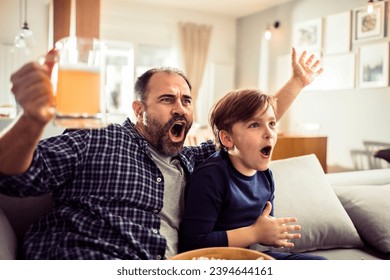 Father and Son Enjoying Snacks and Football at Home - Powered by Shutterstock