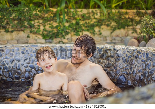 Father and son at family spa relaxing in round\
outdoor fragrant herbal bath, organic skin care, luxury spa hotel,\
lifestyle photo