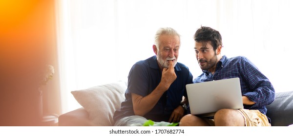 Father and son family time together at home concept. Smiling old father and happy son sitting on sofa using digital laptop computer in living room at home - Shutterstock ID 1707682774