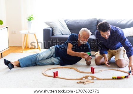 Father and son family time together at home concept. Bearded olf Father and Bearded middle age Son Playing Toy train on floor at home.