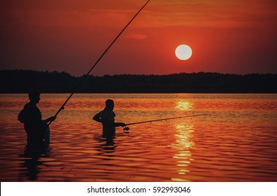 Father And Son Fishing In Lake At Sunset