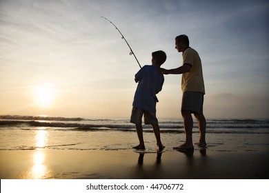 Father and son fishing in ocean surf at sunset.