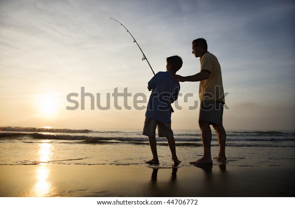Father and son\
fishing in ocean surf at\
sunset.
