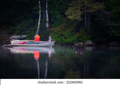 Father And Son Fishing On A Lake In A Boat On A Misty Summer Morning