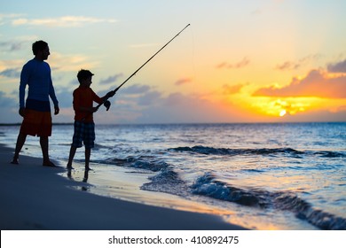 Father and son fishing together in ocean from beach on sunset