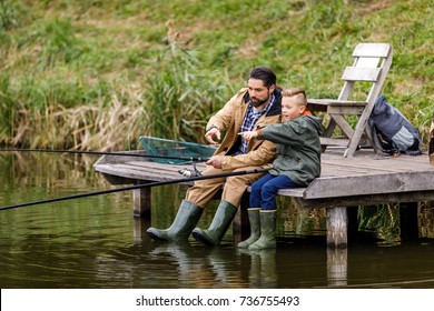 Father And Son Fishing Together With Rods On Wooden Pier At Lake