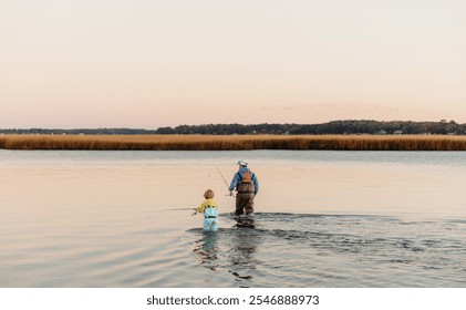 Father and son fishing together at sunset in waders, capturing a special moment of family bonding and outdoor adventure. Perfect stock photo for nature, fishing, family time, and outdoor lifestyle. - Powered by Shutterstock