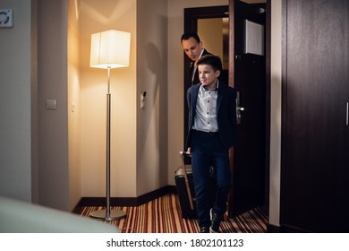 Father and son in formal wear entering a hotel room with suitcases. - Shutterstock ID 1802101123