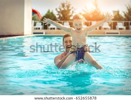 Father and son funny in  water pool under sun light at summer day. Leisure and swimming at holidays.