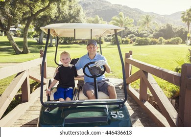 Father And Son Golfing Together On A Summer Day Riding In A Golf Cart Together