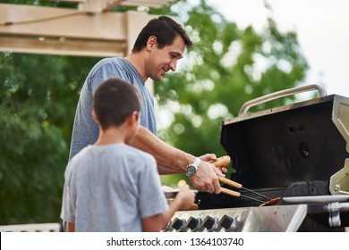 Father And Son Grilling Hot Dogs Together On Backyard Gas Grill