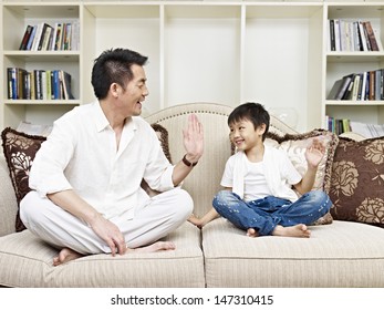 Father And Son Having A Conversation On Couch At Home.