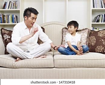 Father And Son Having A Conversation On Couch At Home.