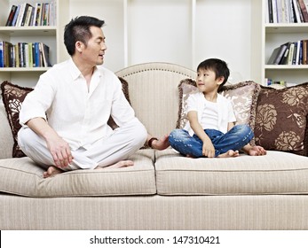 Father And Son Having A Conversation On Couch At Home.