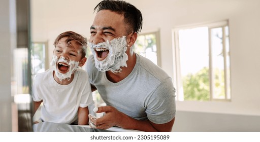 Father and son having fun in a bathroom, laughing happily with shaving foam on their faces. Young single dad taking a moment to bond and share moments of joy with his boy on father's day. - Shutterstock ID 2305195089