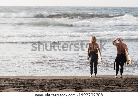 Father and son having fun on the beach at summer sunset for surf training - Focus on backs
