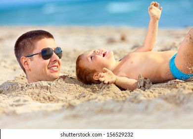 father and son having fun in sand, laughing on the beach