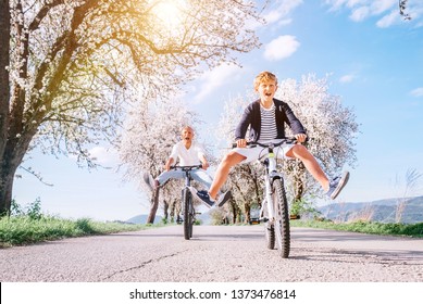Father and son having fun spreading wide legs and screaming when riding bicycles on country road under blossom trees. Healthy sporty lifestyle concept image.